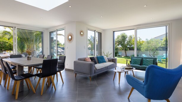 Amplia sala de estar con mesa de comedor, sofás y sillas. Ventanas grandes ofrecen vistas al exterior.