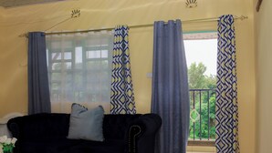 Ein Wohnzimmer mit einem schwarzen Sofa, einem weißen Couchtisch und einem Fenster mit gemusterten Vorhängen.