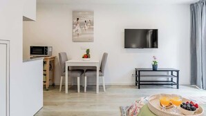A modern hotel room with a dining area, a flat-screen TV, and a breakfast tray with fruits and juice. - Modern & Bright Studio by HostWise (Porto)