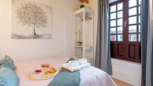 Hotelkamer met een bed, een ontbijttafel, handdoeken, een schilderij van een boom, een wit kastje en een raam met gordijnen.