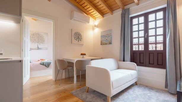 Een gezellige kamer met een witte bank, een klein tafeltje en een raam met gordijnen.