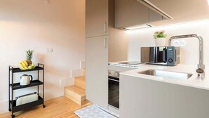Een moderne keuken met een inbouwoven, een magnetron en een spoelbak. Op het aanrecht staat een kleine plant en op een plank een fruitschaal.