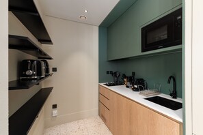 A compact kitchen with a microwave, toaster, and coffee maker on black shelves, a sink, and wooden cabinets.