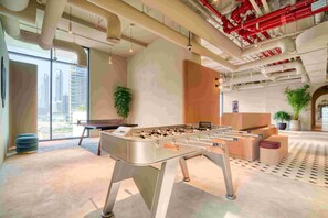 A modern indoor space with a foosball table, large windows, and a view of the cityscape.