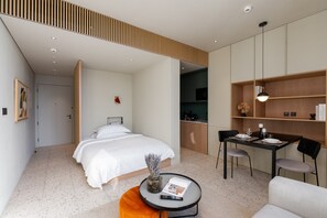 A modern hotel room with a bed, a dining area, and a kitchenette.