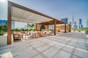 Una terraza en la azotea con mobiliario exterior, vistas del horizonte urbano y una zona cubierta con estructura de madera.