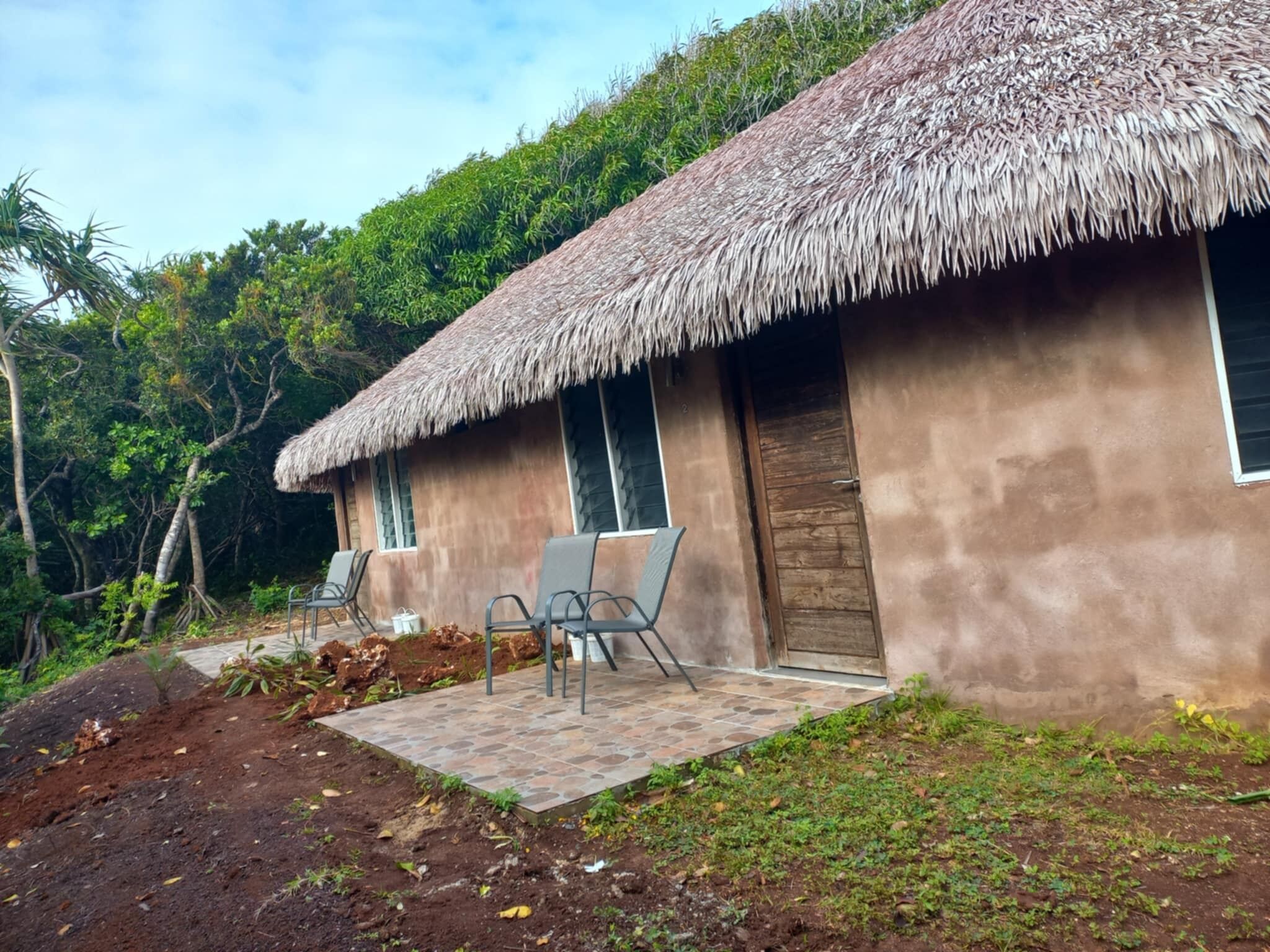 A thatched-roof building with a paved patio and two chairs.