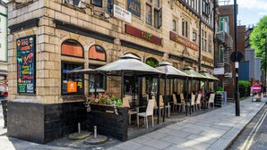 Un restaurant al carrer amb terrassa i un cartell que anuncia un menú de barbacoa i còctels.