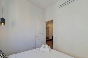 A bedroom with a bed, a door leading to another room, and an air conditioning unit on the wall. - Boutique Home in Setúbal, By Home Match (Setúbal)