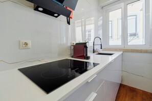 Cozinha moderna com fogão por indução preto, cafeteira e janela com persianas.