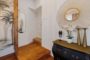 Um corredor com piso de madeira, porta branca, espelho fixado na parede e um objeto decorativo na parede.