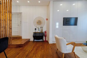 A modern interior with a wooden floor, a black console table with decorative items, a white armchair, and a mounted television. - Boutique Home in Setúbal, By Home Match (Setúbal)