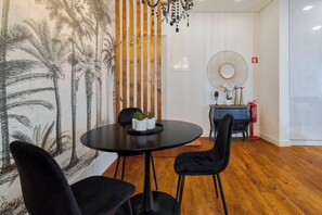 Uma sala de jantar com mesa redonda, cadeiras pretas, parede com painel de plantas tropicais, divisória de ripas de madeira e espelho decorativo.