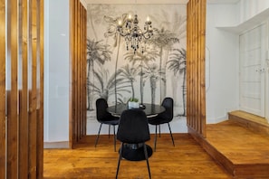 A dining area with a round table, four black chairs, a chandelier, and a wall mural of palm trees. - Boutique Home in Setúbal, By Home Match (Setúbal)