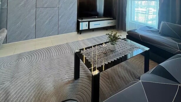 Een moderne woonkamer met een flatscreen televisie, een bijzettafeltje met decoratieve objecten, een bank en een groot raam met gordijnen.