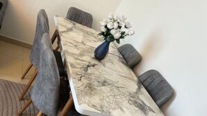 Een eettafel met een marmeren blad, omringd door zes grijze gestoffeerde stoelen. Op de tafel staat een blauwe vaas met witte bloemen.