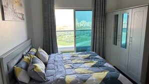 Een slaapkamer met een bed, een garderobe en een groot raam met uitzicht over de stad.