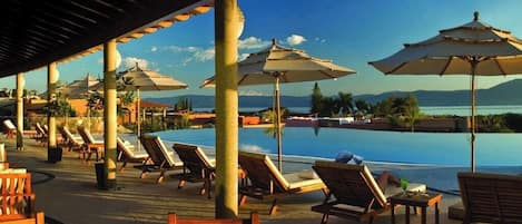 Ein Poolbereich mit Liegestühlen und Sonnenschirmen, mit Blick auf ein Gewässer und entfernte Berge.