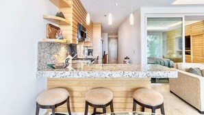 Une cuisine moderne dotée d’un plan de travail en granit, d’étagères en bois et d’un coin bar avec des tabourets.