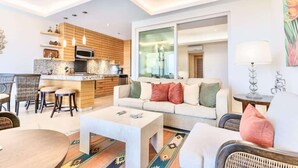Un salon moderne avec un canapé, une table basse et des tabourets de bar. Il y a également un coin cuisine équipé d’un four à micro-ondes et de meubles en bois.