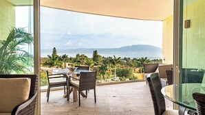 Un balcon agrémenté de meubles en osier, d’une table en verre et offrant une vue sur la mer et les montagnes.