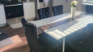 Et moderne køkken med hvide skabe, stålstål-hvidevarer og et spiseområde med et marmorbord og sorte polstrede stole.