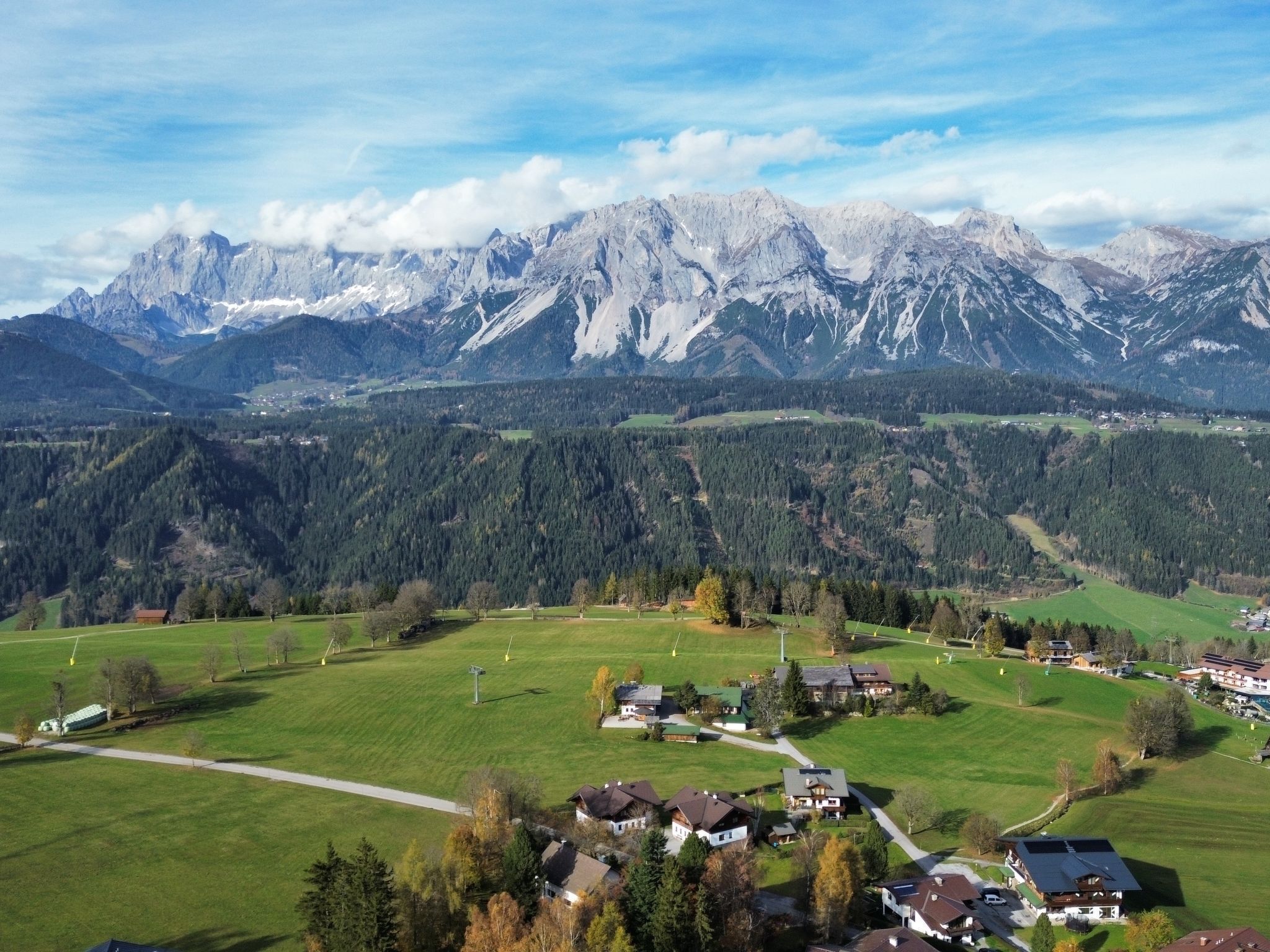 A mountain village with houses and a path leading to a green field.