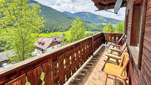 Ein Holzbalkon mit Blick auf eine gebirgige Landschaft, ein Holzstuhl und eine Satellitenschüssel.