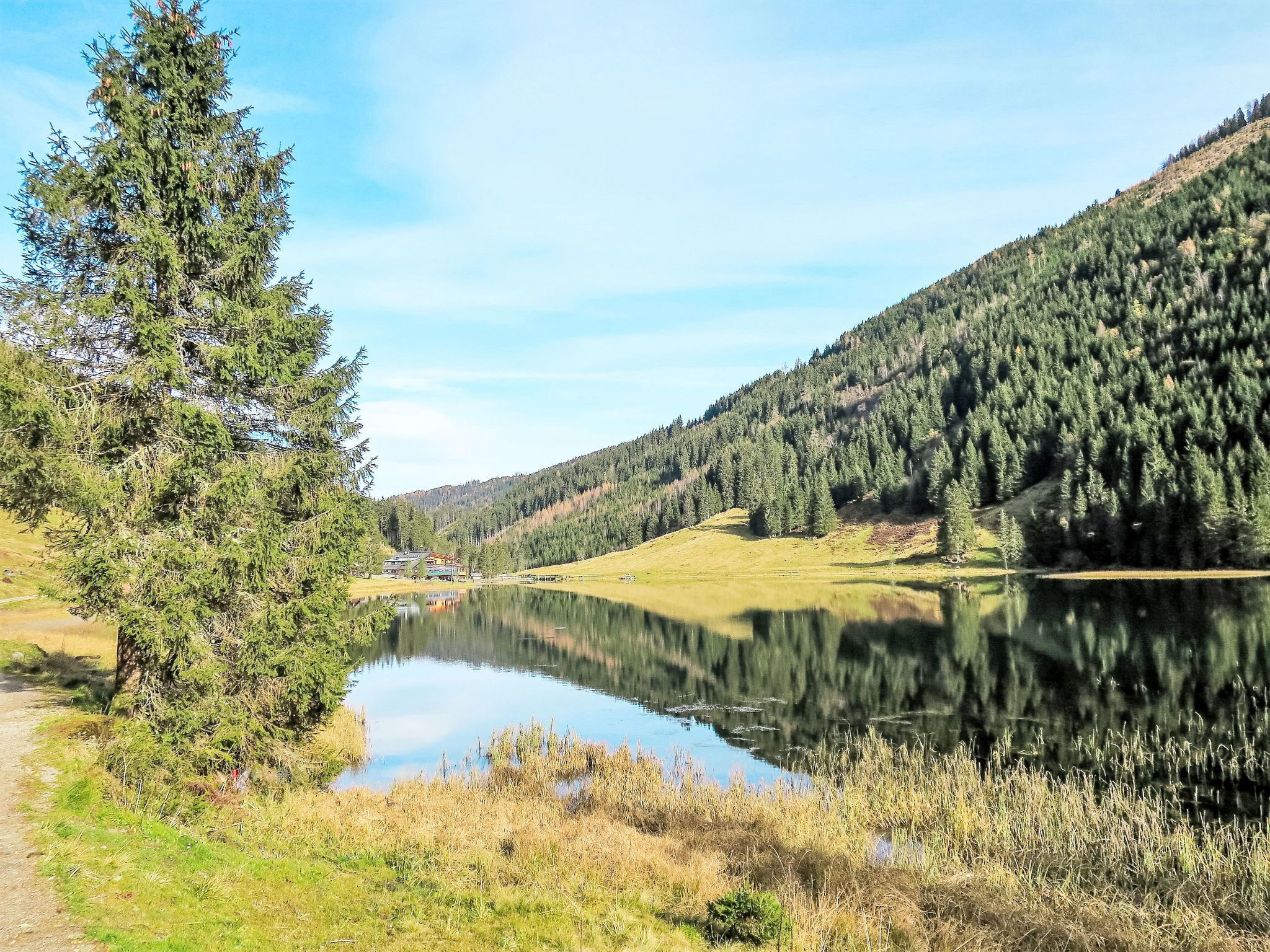 Ein ruhiger See mit einem Pfad, der zu einem Gebäude mit farbenfroher Fassade führt, umgeben von dichtem Wald und Hügeln.