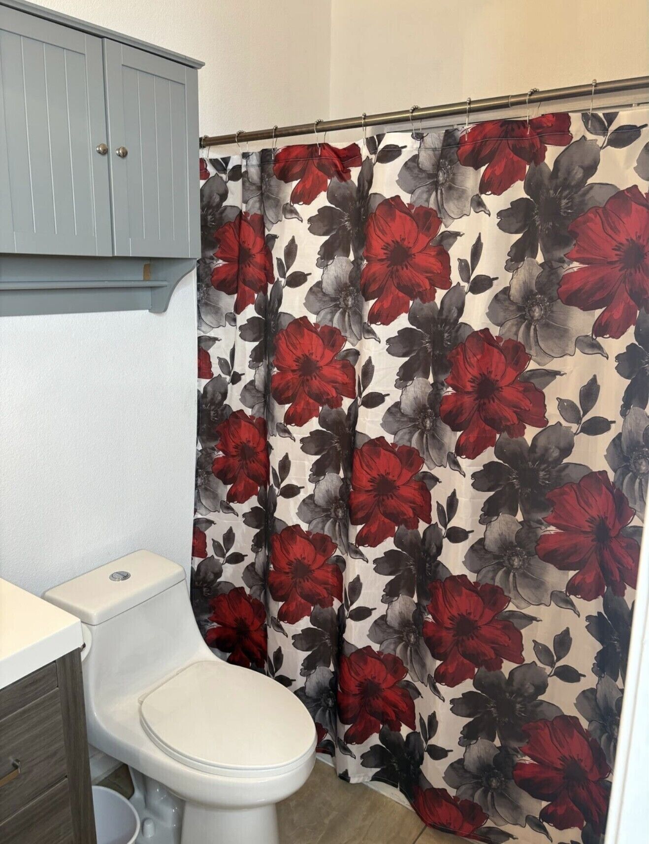 A bathroom with a toilet, a cabinet, and a shower curtain with a floral pattern.