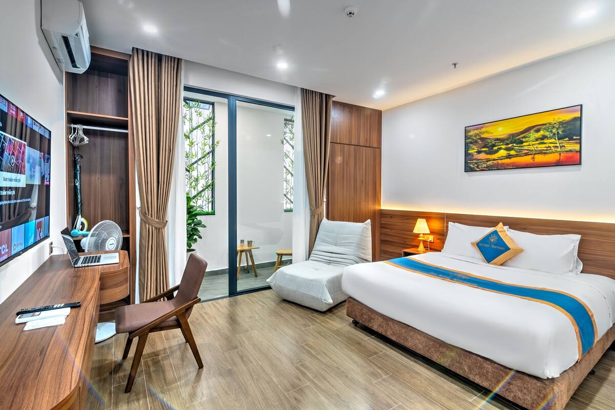 Ein Hotelzimmer mit Bett, Schreibtisch, Stuhl, Fernseher und einem Fenster mit Vorhängen.