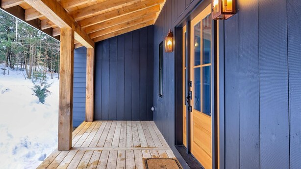 Una terraza de madera con un muro exterior azul oscuro, techo de madera y dos faroles fijos a la pared.