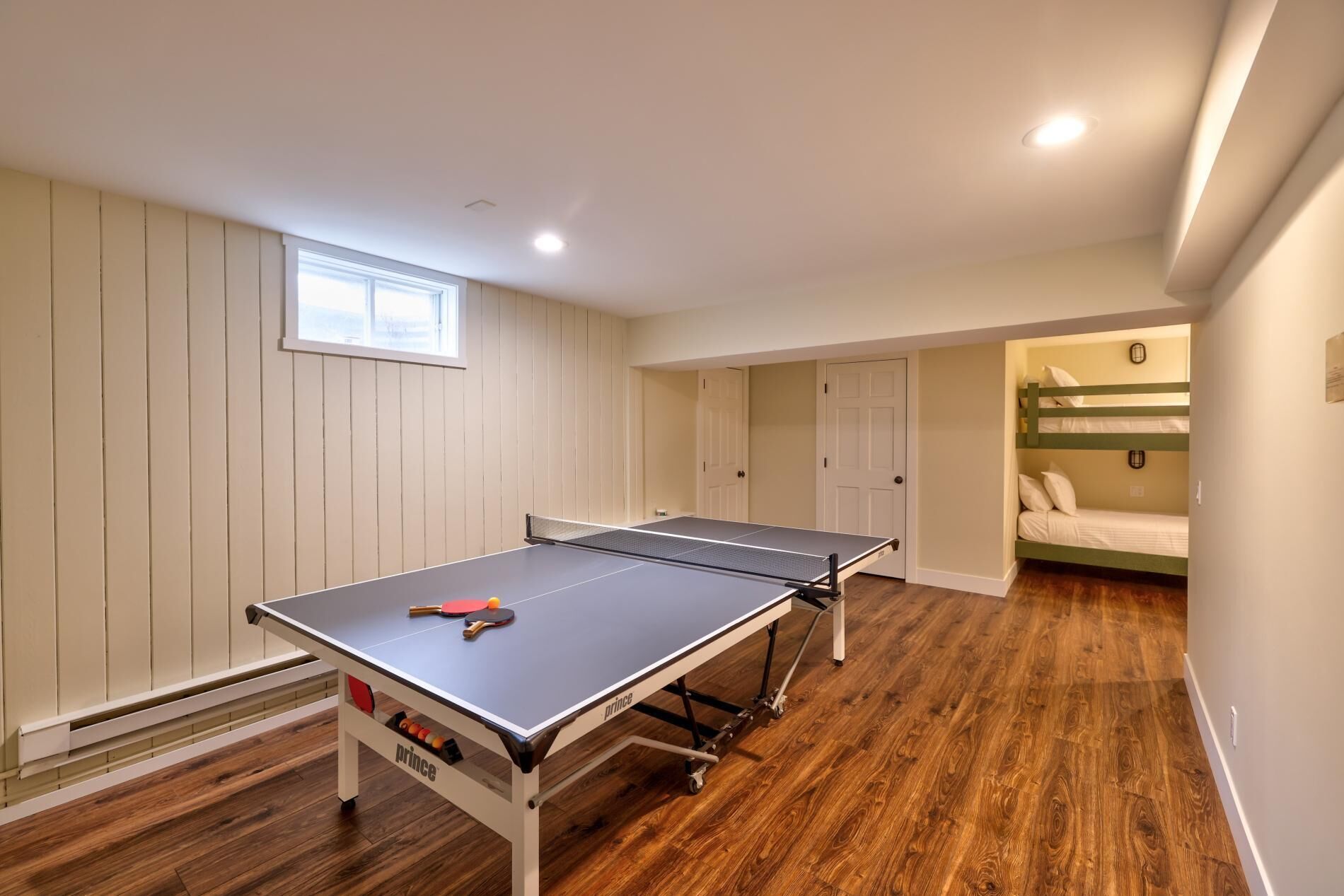 A room with a ping pong table, a bunk bed, and a window.