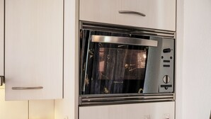 A kitchen with a built-in oven, wooden utensils in a jar, and a towel hanging on hooks. - Haus Europa by Interhome (Kandersteg)