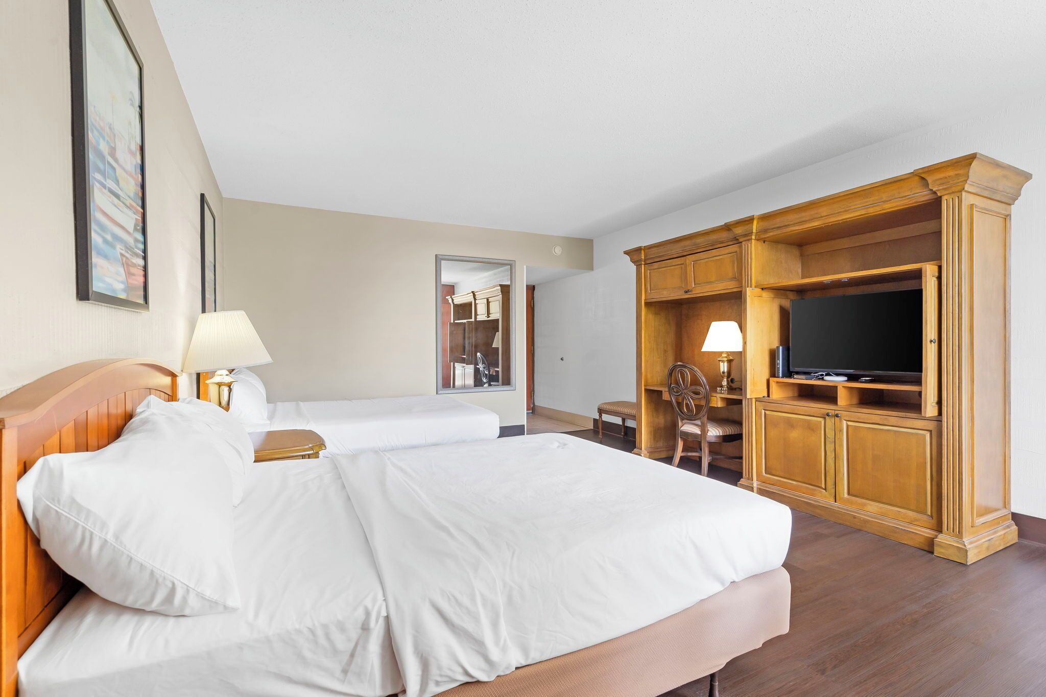 A hotel room with two beds, a television, wooden furniture, and a mirror.