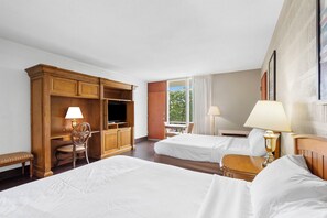 A hotel room with two beds, a desk, a TV, and a window with curtains.