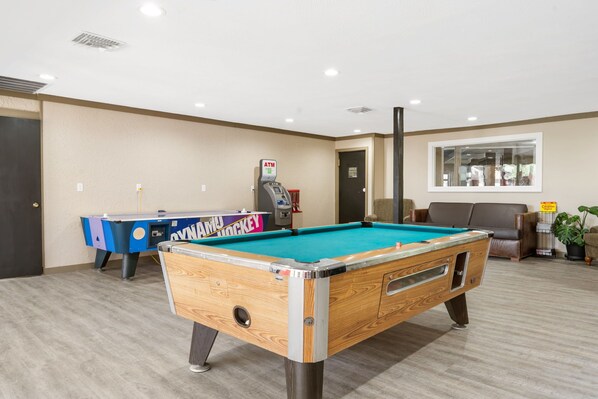 Una mesa de billar en una habitación con mesa azul y morada, un cajero automático, un sofá y una ventana.