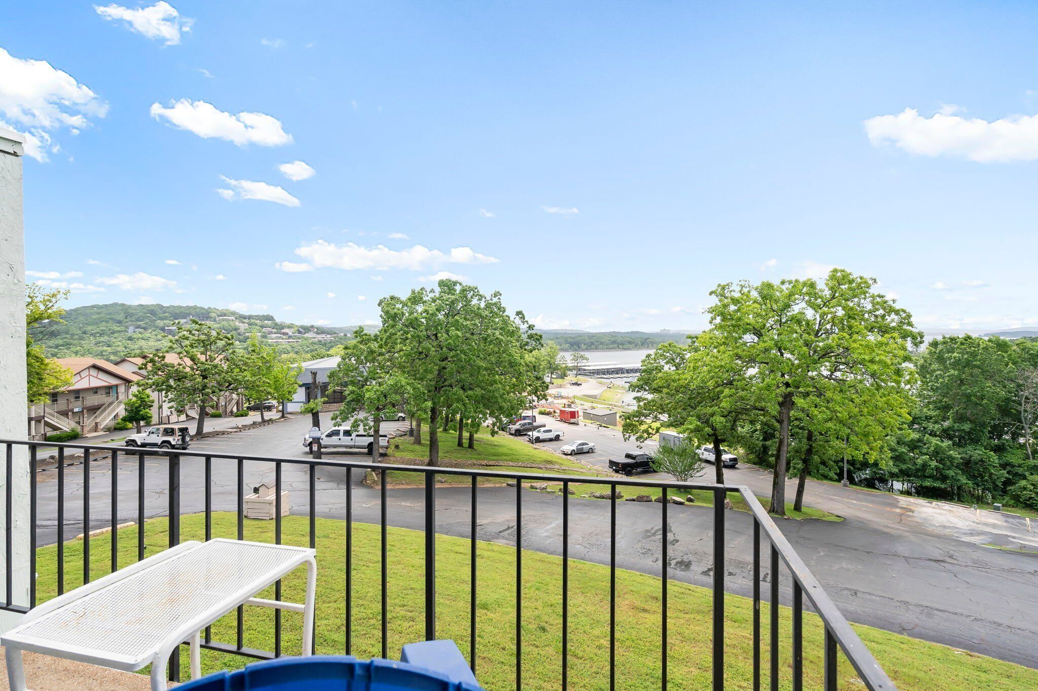 A balcony with a view of a parking lot, trees, and a distant building.