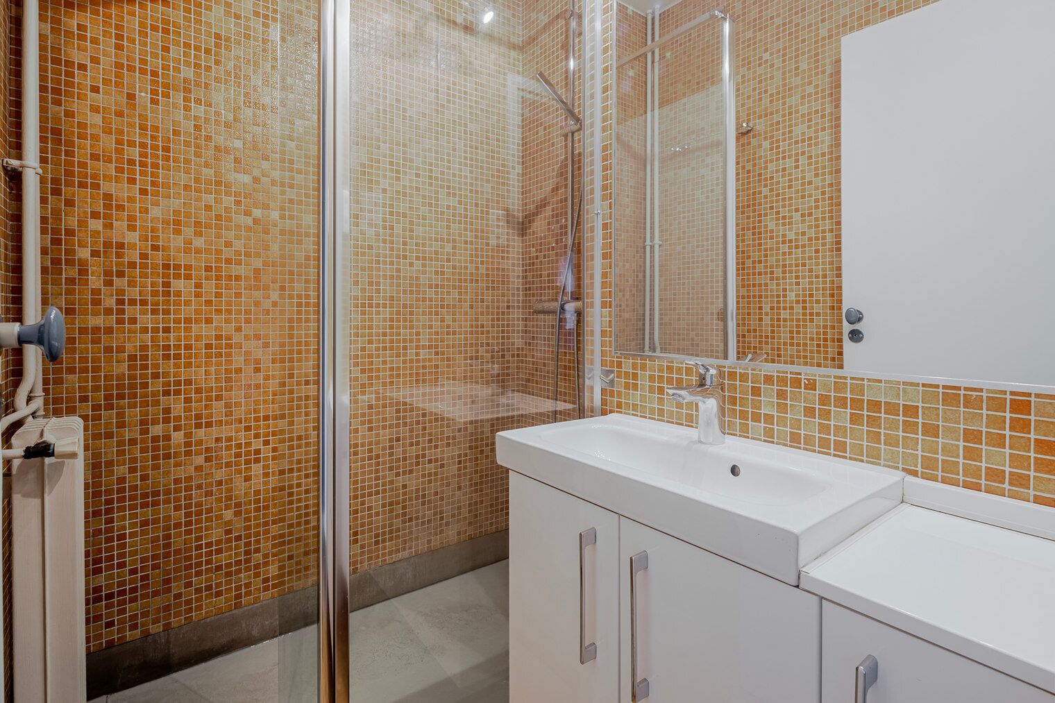 Un bagno con parete rivestita in piastrelle, cabina doccia, lavandino e specchio.