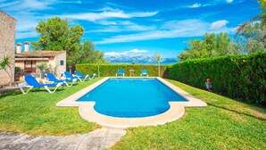 Une piscine rectangulaire bordée de pierres, entourée d’une pelouse bien entretenue et de chaises longues bleues.