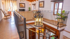 Un vaste espace de vie doté d’un haut plafond, de poutres apparentes, d’un balcon avec une balustrade et d’une lanterne suspendue.