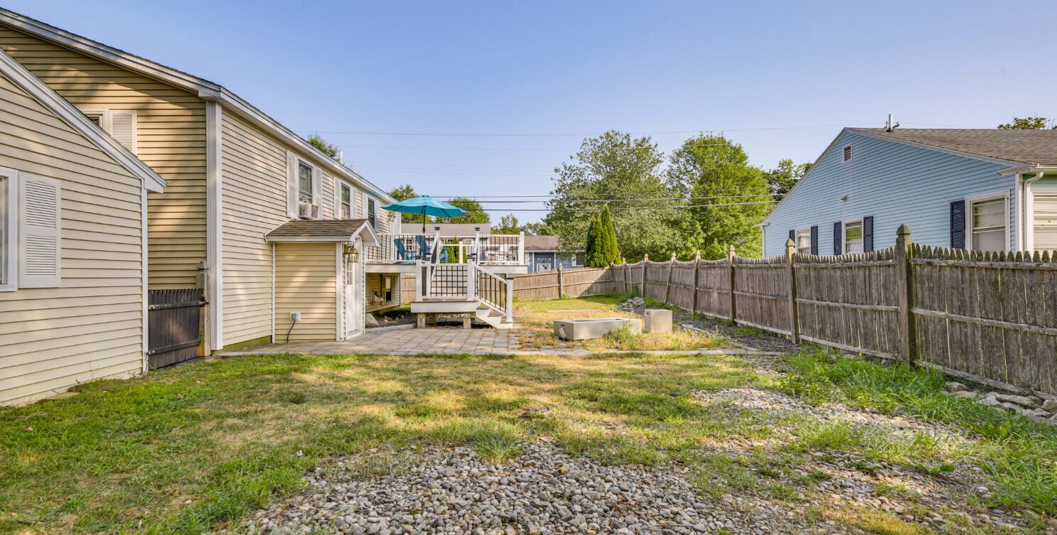 A residential backyard with a wooden deck, a small patio, and a fenced area.