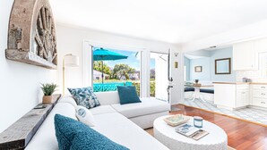 Amplia sala de estar con un sofá blanco, cojines azules, una mesa de centro redonda y vistas al exterior.