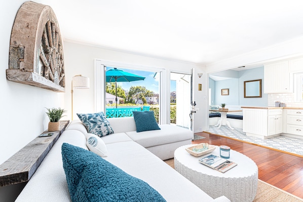 A spacious living room with a white sofa, blue cushions, a round coffee table, and a view of the outside.