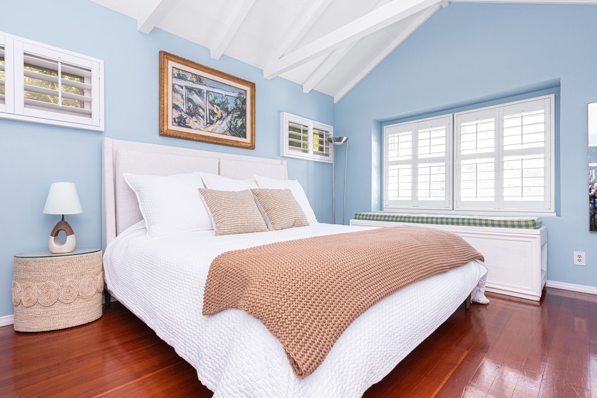 A bedroom with a large bed, a window, and a painting on the wall.