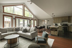 Un vaste salon doté d’un haut plafond, de grandes fenêtres, d’un coin repas et d’une cuisine avec des meubles en bois.