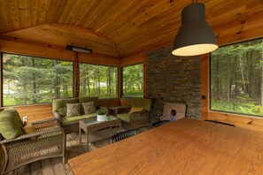 A cabin interior with a dining table, seating area, and large windows offering forest views.