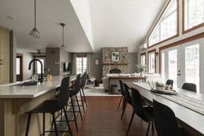 Une cuisine spacieuse dotée d’un îlot central, un coin repas avec une longue table et un espace salon confortable avec une cheminée.