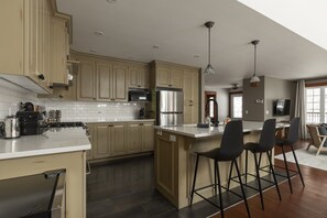 A modern kitchen with a central island, bar stools, and a dining area with a TV. - Chalet: Fireplace • Game Room • HotTub • Ski 2min (Les Laurentides Regional County Municipality)