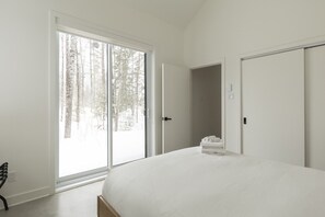 Een slaapkamer met een groot bed, een schuifdeur naar een besneeuwd bos en een kledingkast.